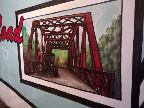 A mural depicting a red bridge with a vintage car on a road, surrounded by green trees.