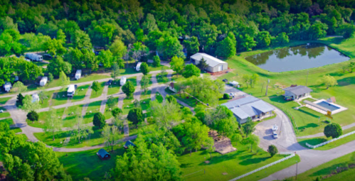 Aerial view of a green campground with RVs, a pond, and various trees and buildings.