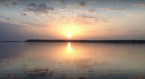 A serene sunset over a calm lake, with soft clouds reflecting on the water's surface.