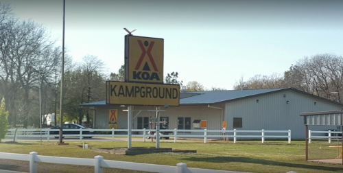 Sign for KOA Campground with a building in the background and a grassy area in front. Trees line the background.