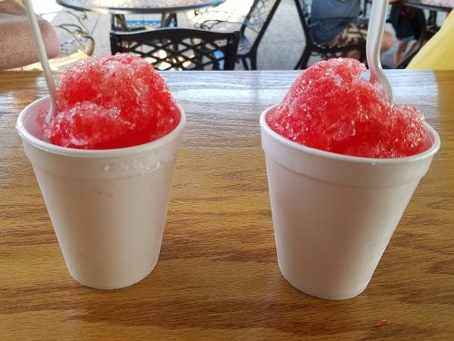 Two white cups filled with bright red shaved ice, sitting on a wooden table.
