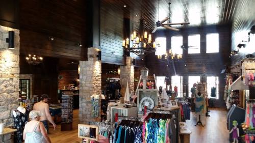 A spacious retail store with stone walls, wooden beams, and various clothing displays, illuminated by chandeliers.