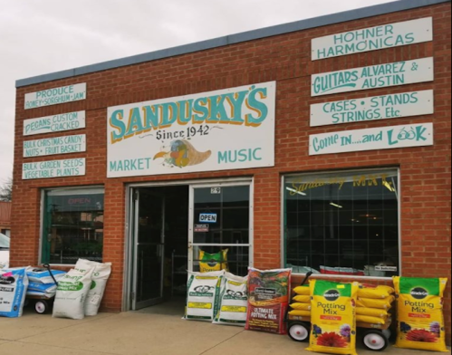 Exterior of Sandusky's Market, featuring produce, music instruments, and bags of potting mix outside the store.