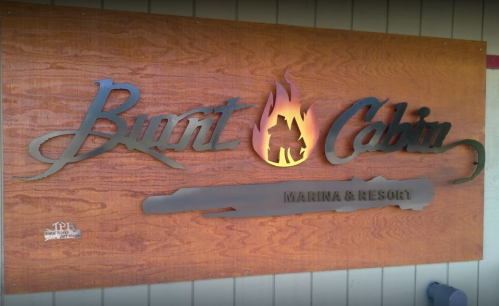 Sign for Burnt Cabin Marina & Resort, featuring a wooden background and metal lettering with a flame design.