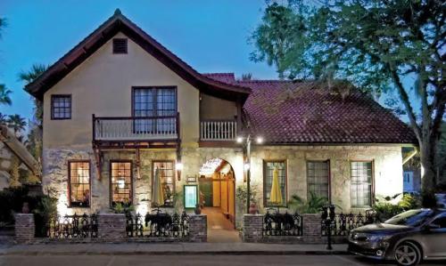 A charming two-story house with a red tile roof, stone walls, and a welcoming entrance, surrounded by trees at dusk.