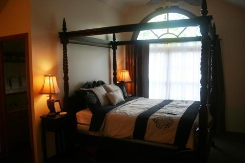 A cozy bedroom featuring a four-poster bed, warm lighting, and large windows with sheer curtains.