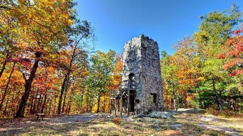 A stone tower surrounded by vibrant autumn trees under a clear blue sky.