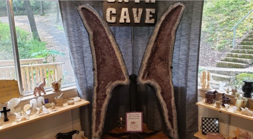 A large amethyst geode display with decorative items and shelves in a cozy shop setting.