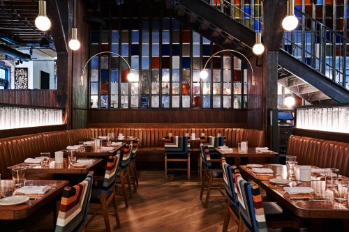 A stylish restaurant interior featuring wooden tables, striped chairs, and colorful stained glass windows.