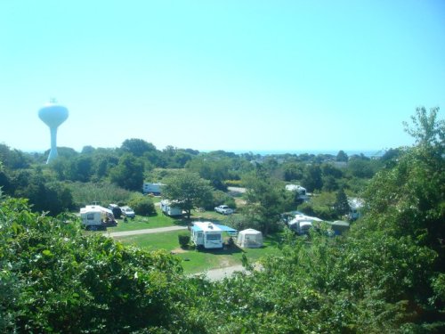 A scenic view of a campground with several RVs, surrounded by trees and a water tower in the background under a clear blue sky.