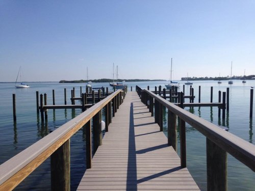 A wooden pier extends into calm water, with sailboats moored nearby under a clear blue sky.