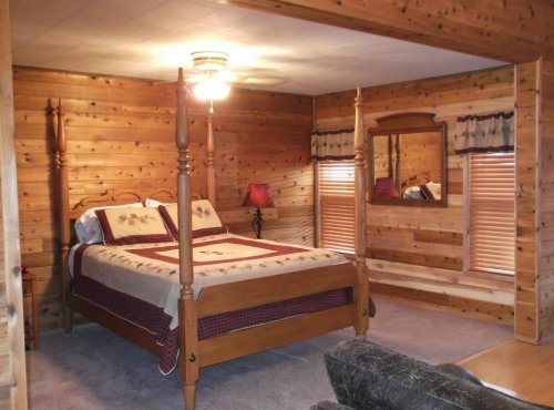 Cozy wooden bedroom with a four-poster bed, warm lighting, and rustic decor.