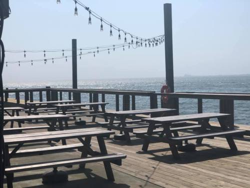 A wooden deck with picnic tables overlooking a shimmering body of water, adorned with string lights.