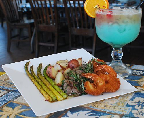 A plate of grilled steak, asparagus, roasted potatoes, and fried shrimp, accompanied by a colorful cocktail.