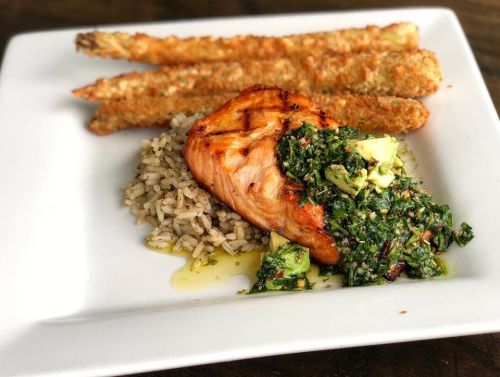 Grilled salmon topped with avocado salsa, served with rice and crispy asparagus on a white plate.