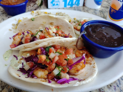 Three shrimp tacos topped with cabbage, tomatoes, and onions, served with a side of black beans.