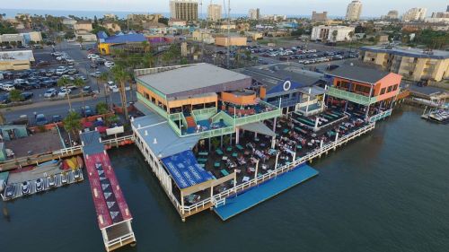 Aerial view of a colorful waterfront restaurant with outdoor seating, surrounded by water and nearby buildings.
