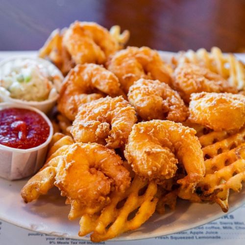 A plate of crispy fried shrimp served with waffle fries and a side of coleslaw and dipping sauce.