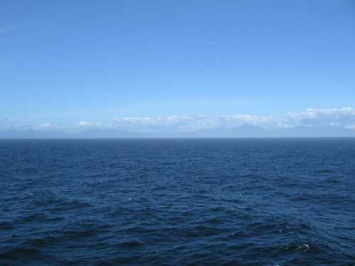 A vast ocean under a clear blue sky, with distant mountains barely visible on the horizon.