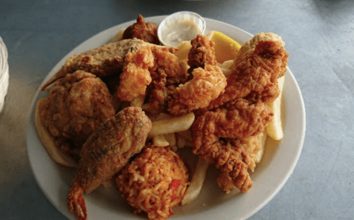 A plate of assorted fried seafood and chicken, served with fries and a small cup of dipping sauce.