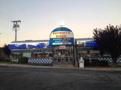 A classic diner with a blue and white checkered exterior, neon lights, and a sign reading "Patriots Diner - Open."