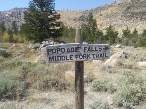 Wooden signpost indicating directions to Popo Agie Falls and Middle Fork Trail in a mountainous landscape.