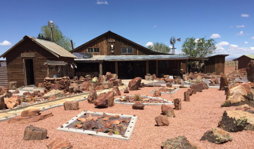 A rustic wooden building surrounded by large colorful rocks and a gravel landscape under a blue sky.
