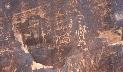 Petroglyphs carved into a dark rock surface, depicting various figures and symbols in an ancient style.