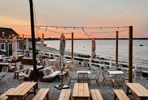 Outdoor seating area by the beach at sunset, with string lights and a view of the water.