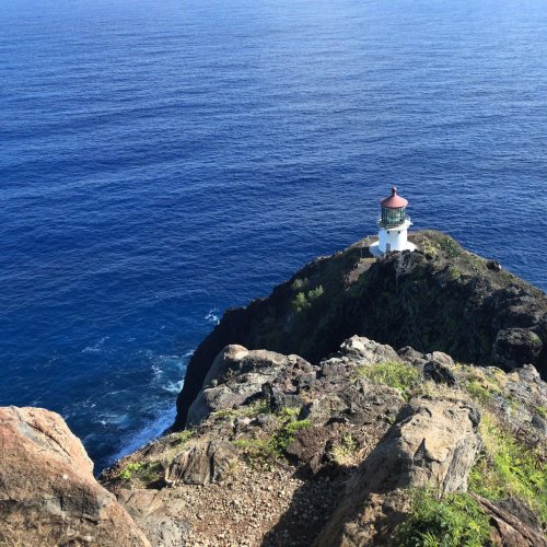 A lighthouse perched on a rocky cliff overlooking a deep blue ocean under a clear sky.