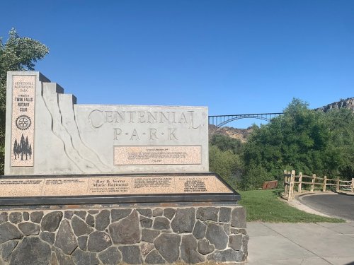 A stone monument for Centennial Park, with a bridge visible in the background and trees lining the path.