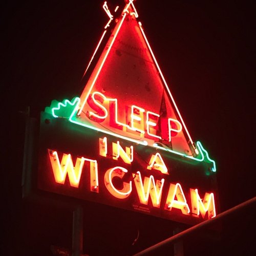 Neon sign reading "Sleep in a Wigwam" with a triangular design, illuminated against a dark night sky.