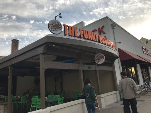 Exterior of The Funky Brunch restaurant, featuring colorful seating and a sign, with two people walking by.