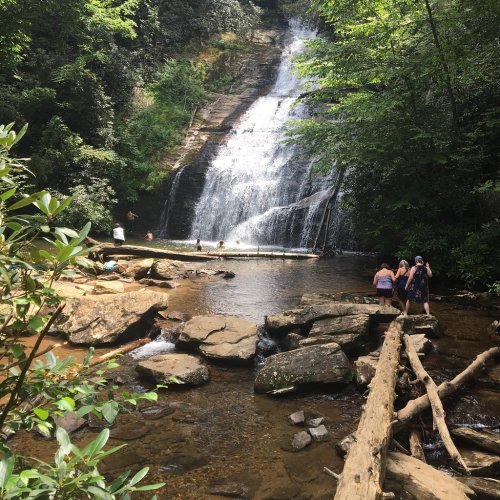 A scenic waterfall surrounded by lush greenery, with people enjoying the water and rocky terrain.