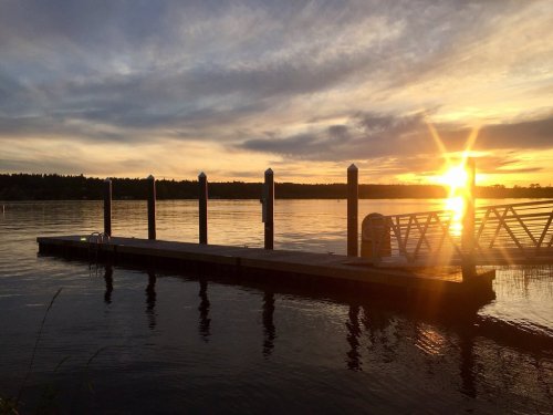 A serene sunset over a calm lake, with a wooden dock extending into the water and a starburst effect from the sun.