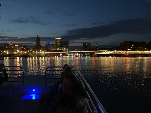 A nighttime view from a boat, showcasing city lights reflecting on the water and a skyline in the background.