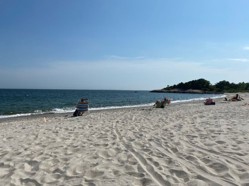 A sunny beach scene with people relaxing on the sand and gentle waves lapping at the shore.