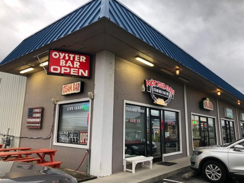 Exterior of a seafood restaurant with signs for "Oyster Bar Open" and "Live Crab," featuring a blue roof and parking area.