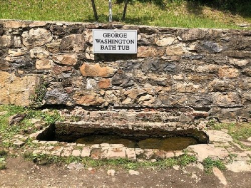 A stone structure with a sign reading "George Washington Bath Tub" above a small, water-filled basin.