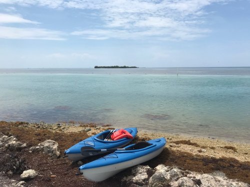 Two blue kayaks on a rocky shore with calm turquoise water and a small island in the distance under a cloudy sky.