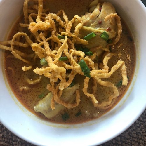 A bowl of curry soup with chicken, topped with crispy fried noodles and green onions.