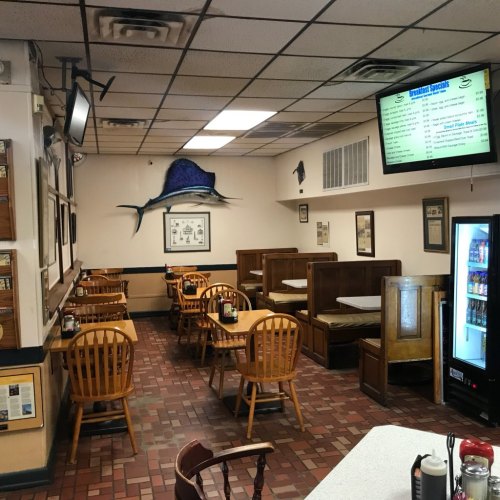Interior of a casual dining restaurant with wooden tables, booths, and a menu board on the wall.