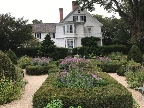 A white house surrounded by neatly trimmed hedges and colorful flower beds in a serene garden setting.