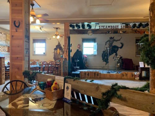Interior of a rustic restaurant with wooden decor, a stage for performances, and tables set for dining.
