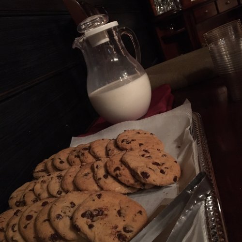 A tray of chocolate chip cookies next to a glass pitcher of milk on a table.