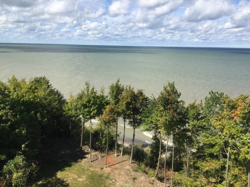 A serene view of a lake with gentle waves, framed by green trees under a partly cloudy sky.