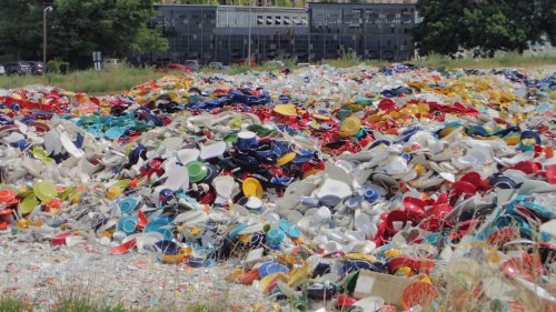 A large pile of colorful broken dishes and pottery scattered across a grassy area, with buildings in the background.