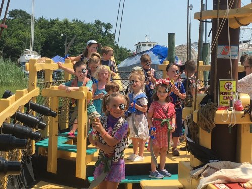 A group of children playing on a pirate ship playground, smiling and enjoying their time outdoors.