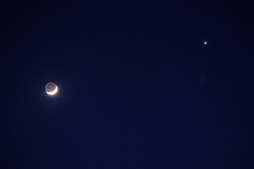 A crescent moon and a bright star shine in a dark night sky, surrounded by scattered stars.