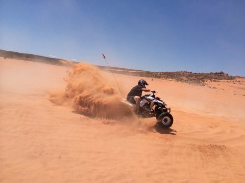 A person riding an ATV through a sandy desert, kicking up dust and sand in a dynamic motion.